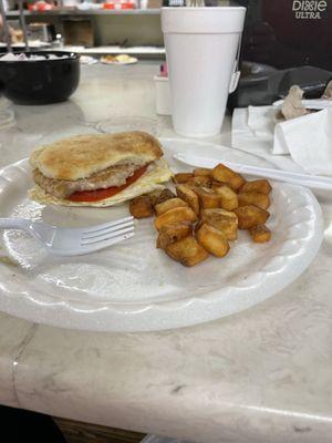 Tenderloin sandwich with fried egg and tomato with a side of fried potatoes.