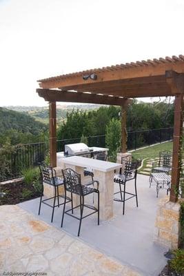 Outdoor kitchen designed with stone accented by wooden pergola.