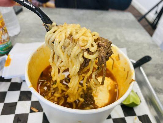 Birria ramen served with beef, sweet corn, diced onions, cilantro, scallions and lime