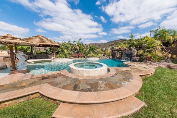 Tropical beach entry custom swimming pool with a perimeter flow spa, grotto, rock slide, and waterfalls. Outdoor kitchen with swim up bar.