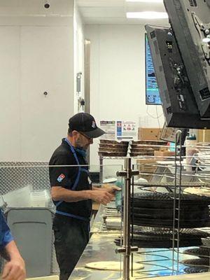 An employee not wearing a mask and making pizzas for the public.