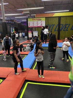 Children sitting on trampolines in back while others walk on pads looking for one to jump on.