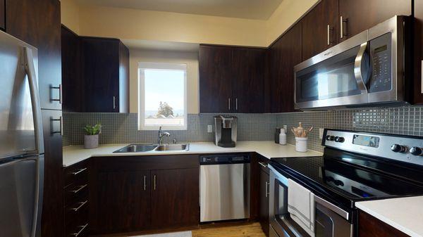 Staged kitchen featuring hardwood-style vinyl flooring, stainless steel appliances, and quartz countertops.