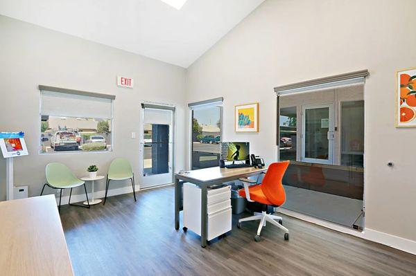 Leasing office area with plank flooring, waiting area with chairs, and a desk with an orange chair