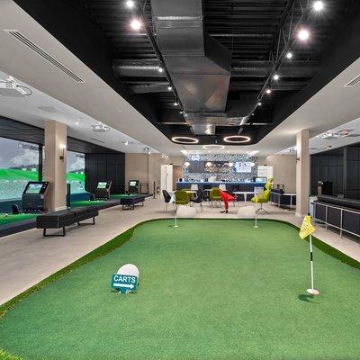 Our lobby area with a practice green, rest area and bar surrounded by driving range bays and course play bays.