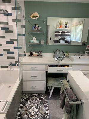 Master Bathroom counter, glass shelving, LED mirror, vanity, pony wall enclosing toilet with reflection above toilet seen in mirror