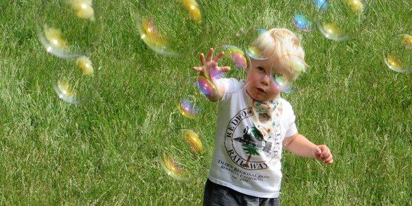 A kid reaches toward a shower of bubbles