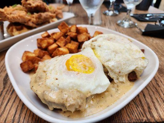 Biscuits and gravy topped with eggs and served with house potatoes