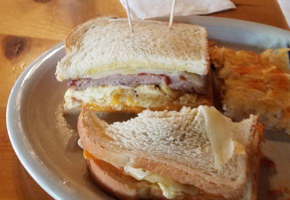 Sourdough sandwich with sausage and hashbrowns on the side.