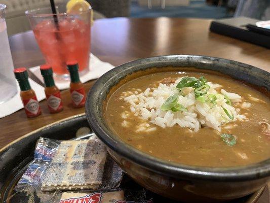 Amazing gumbo accompanied by three tiny hot sauce bottles and a Bourbon on the Bayou