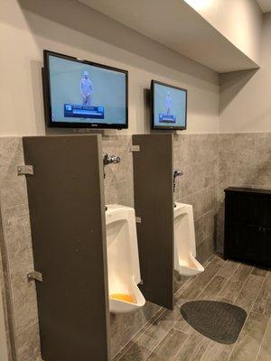 TVs above the urinals inside the men's restroom.