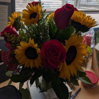 The bouquet consists of 6 sunflowers and 6 red roses in a glass vase.