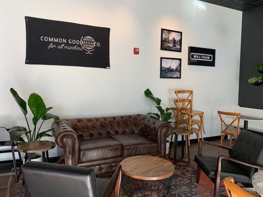 The couch and chair set up in the building along with their logo and some photos and plants