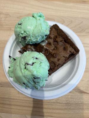 Two scoops of mint chocolate chip ice cream served over a well proportioned piece of chocolate / chocolate chip brownie.