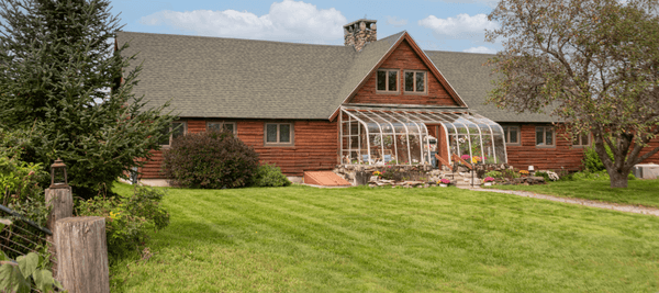 Log cabin lodge with greenhouse attached and expansive lawn.