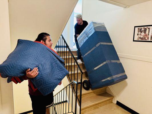 A mover expertly guides furniture down stairs, showcasing agility and precision in the task.