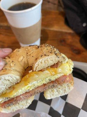 The perfect Bacon, Egg and Cheddar with tomato and black pepper on a toasted everything bagel with butter. Large black coffee.