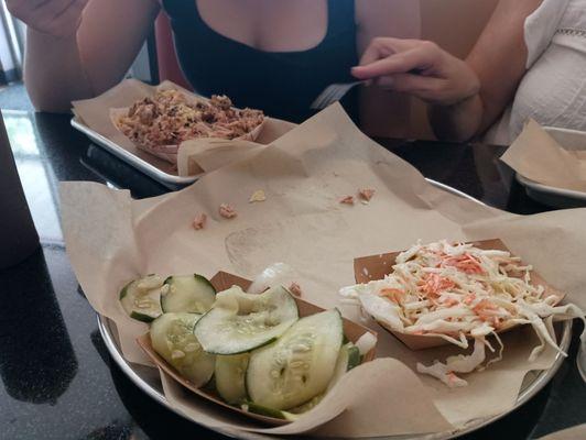 Plain pulled chicken in tray furthest away, with cucumbers and Cole slaw