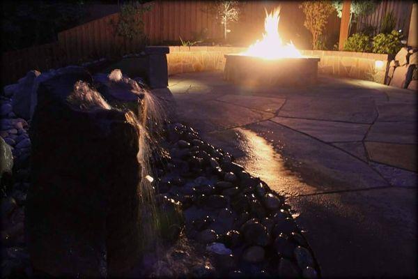 Flagstone patio with seating wall, gas fire pit, stone bubbler water feature and night lighting