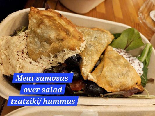 Meat samosas over salad with hummus and tzatziki