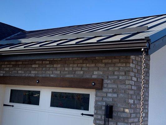 Gutters and rain chain with snow guard on a metal roof.