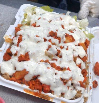 Chicken over rice with salad , white sauce on top .