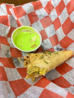 Half eaten Chicken Samosa with green sauce (cilantro?)