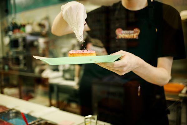 A donut being topped with rainbow sprinkles