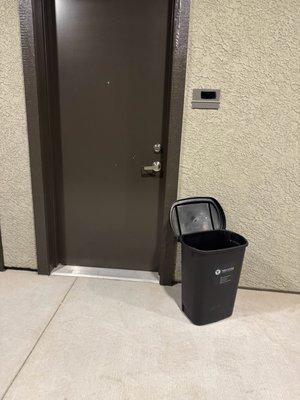 This trash can has been out for three days, is dirty, and emits a strong odor. Residents have to pass by it to reach their units.