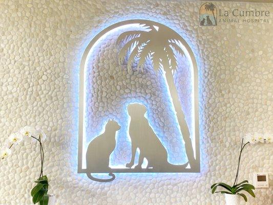 Pictured: custom metal LCAH logo sign lit light blue on white stone wall framed by two white orchids.