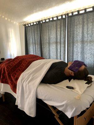 Clients relax laying face up on a massage table with eyes covered for most of the session.