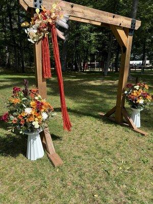 Autumn themed floral arrangement, rented white stands, complimenting bride's own wooden device and artificial decoration/ribbon.