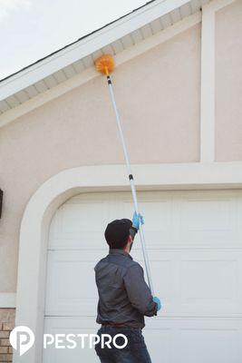 A Pest Pro technician de-webbing the eaves of a home.