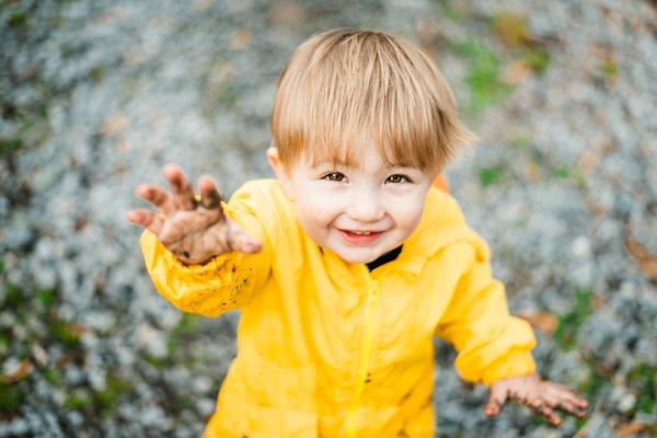 Toddler shows the camera his muddy hands after playing in the rain.