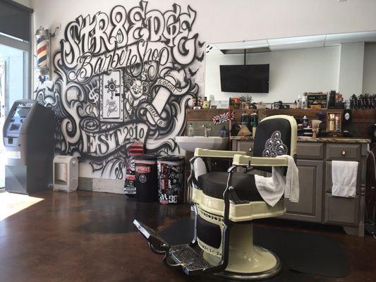 A picture of the inside where the wall is spray painted one of the vintage barber shop chairs, plus a granite countertop behind.