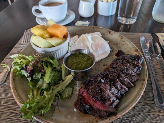 Steak and eggs with mixed greens, pesto sauce and fruit