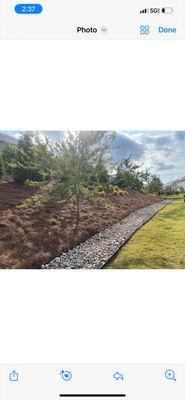 Installed pine needles and river rock bed with metal edging