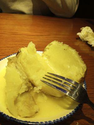 Half baked potato with butter running on the saucer.