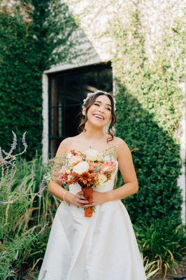 Cheerful bride smiles with bouquet of flowers in front of ivy covered venue