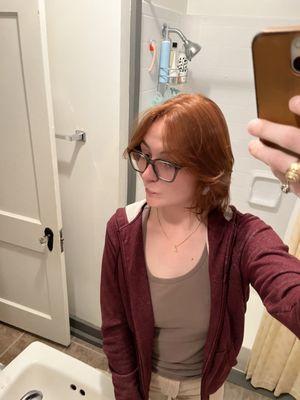 Woman smiles in front of mirror, showing red/orange haircut