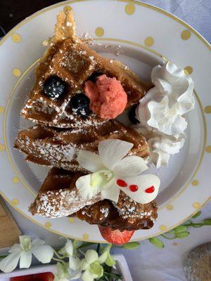 Chicken and waffles topped with strawberry butter and edible orchids.