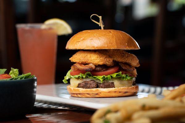 The Smokehouse Burger is a 1/2 lb wagyu blend burger stacked tall with bacon, cheddar, and our hand-battered onion rings.