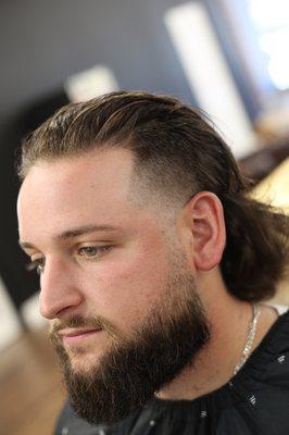 Burst fade, layered back scissor cut with a tapered beard trim (classic Mullet)