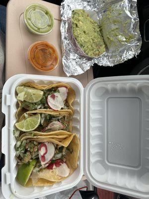 Three chicken tacos with onion, cilantro, radish and limes with side of guacamole and their green and red sauce.