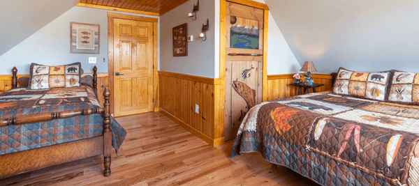 Room with a queen bed and a twin bed with wooden floors and a door carved with a fish.