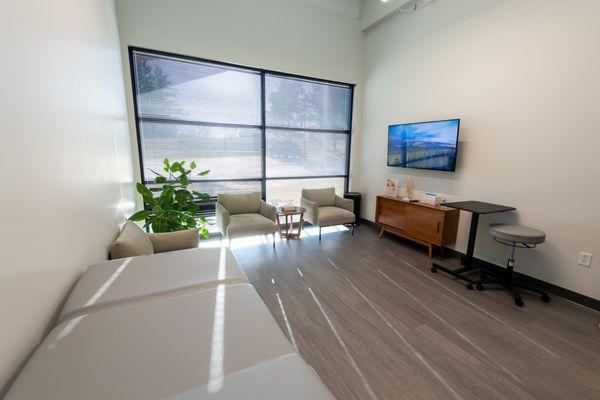 Exam room at Vertrae® with sofa chairs, large window, and television