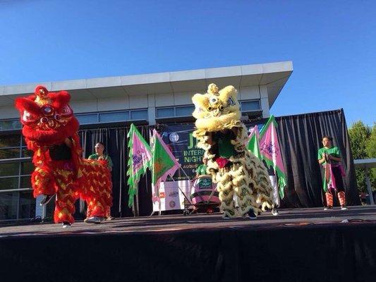 Red and gold lion dance performance on stage for Jade District Market event. White Lotus Dragon & Lion Dance - Portland, OR