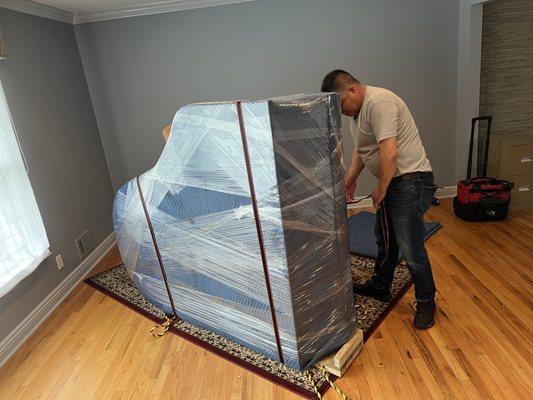 Grand piano covered with furniture blankets and plastic wrap.