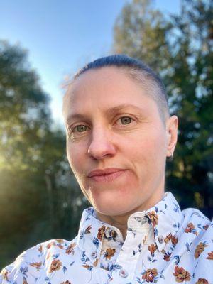 A headshot portrait of Nik Kurtz, a white queer trans non-binary person with eyes directed at the camera.  They offer Esalen Massage.