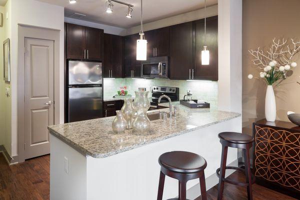 Kitchen with espresson cabinetry, granite coutertops, stainless-steel appliances, and breakfast bar with pendant lighting